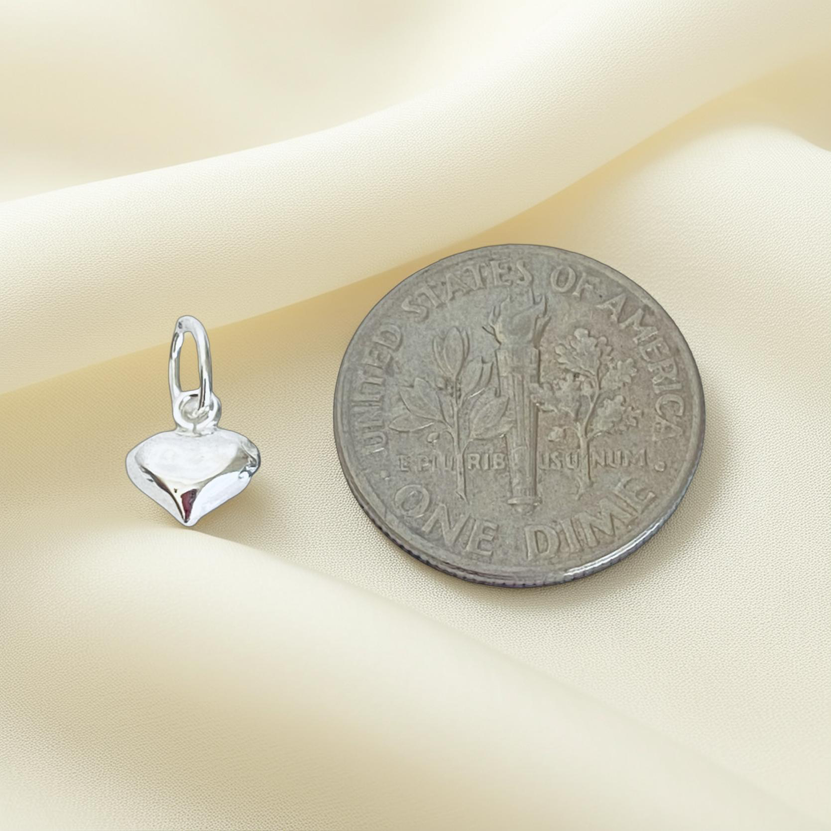Silver heart-shaped pendant next to a U.S. dime on a beige background